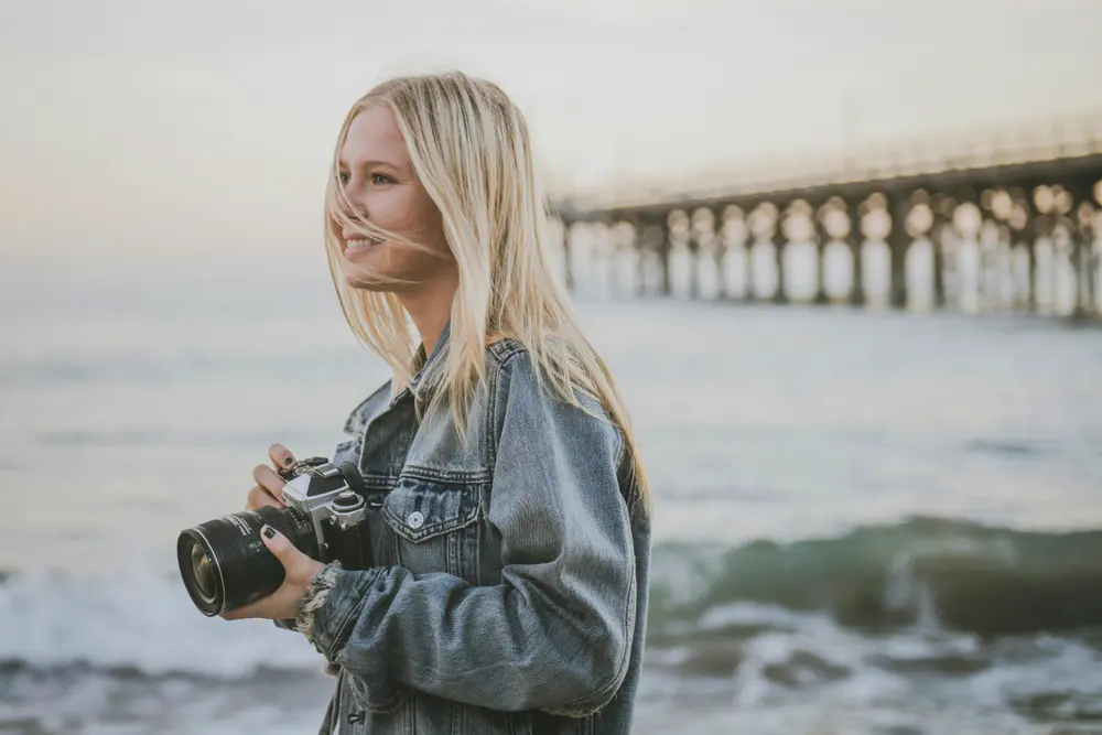 A photographer holding a camera on the beach, without a watermark